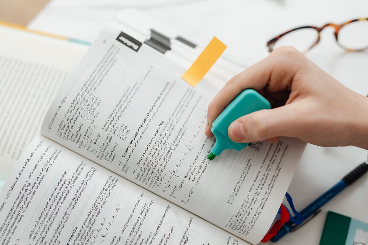 About Close-up of a hand using a highlighter on an open textbook, focusing on key information.