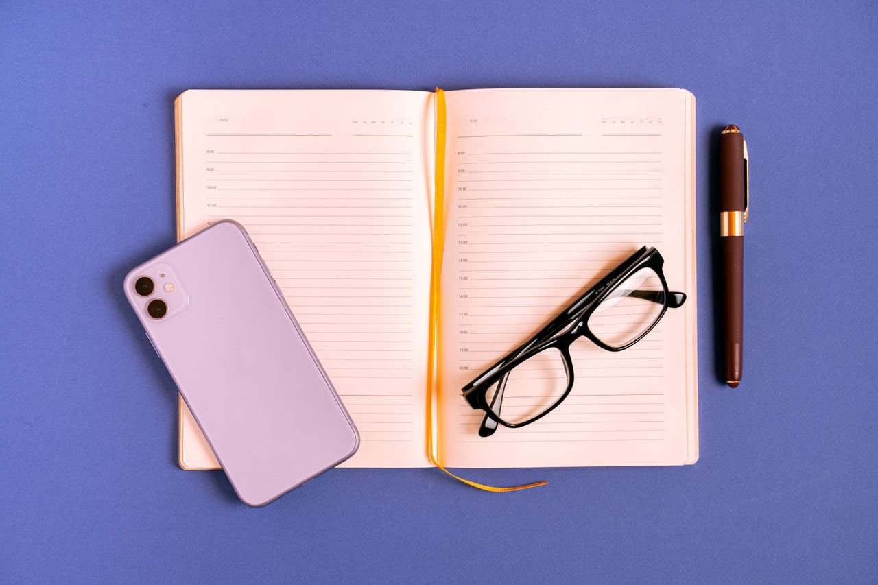 Open notebook with eyeglasses, smartphone, and pen on a blue background.