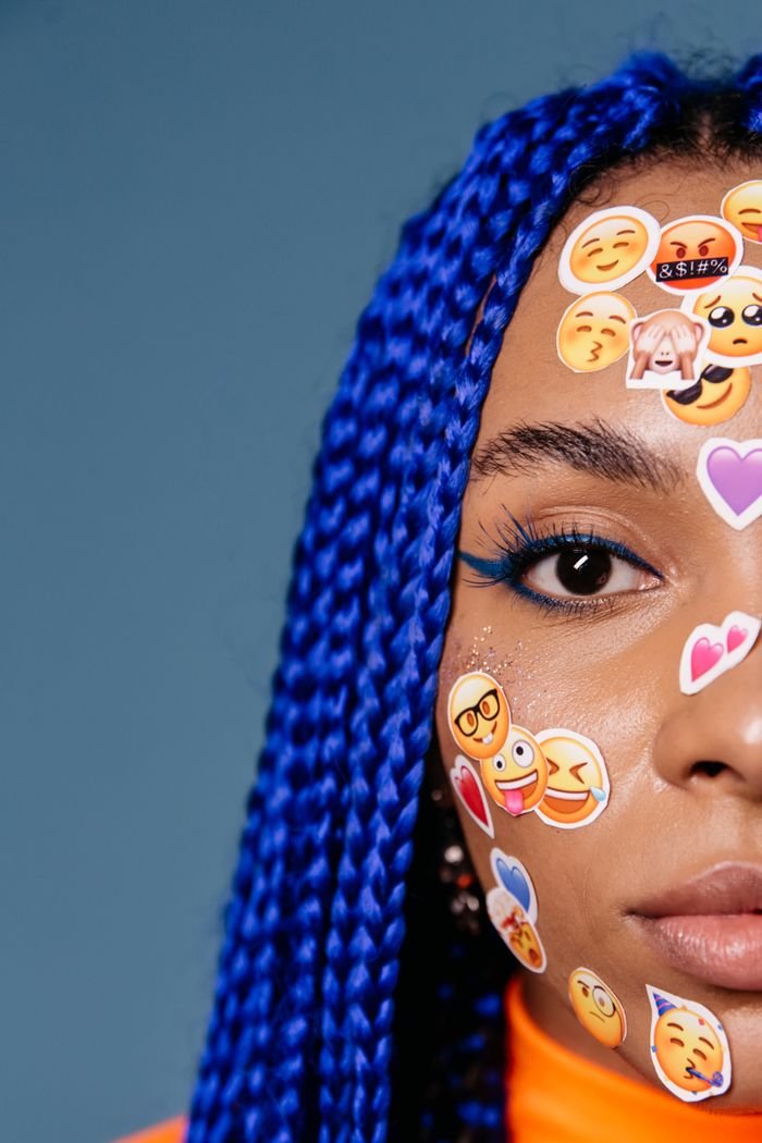 The Art of Drawing Readers In: Your attractive post title goes here Close-up of a woman with blue braided hair and emoji stickers on her face, expressing creativity and emotions.